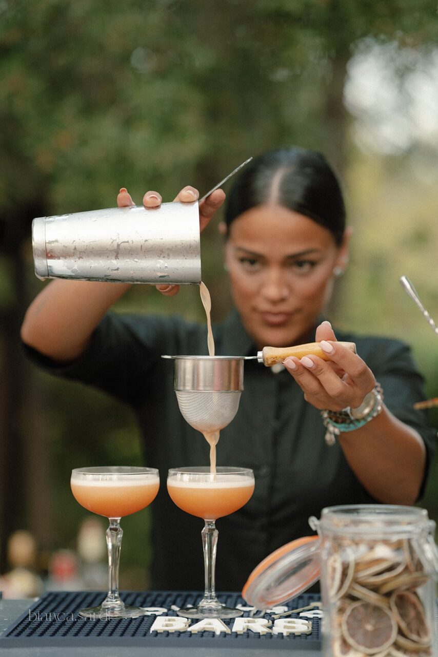 A woman pouring drinks at a bar using a shaker.